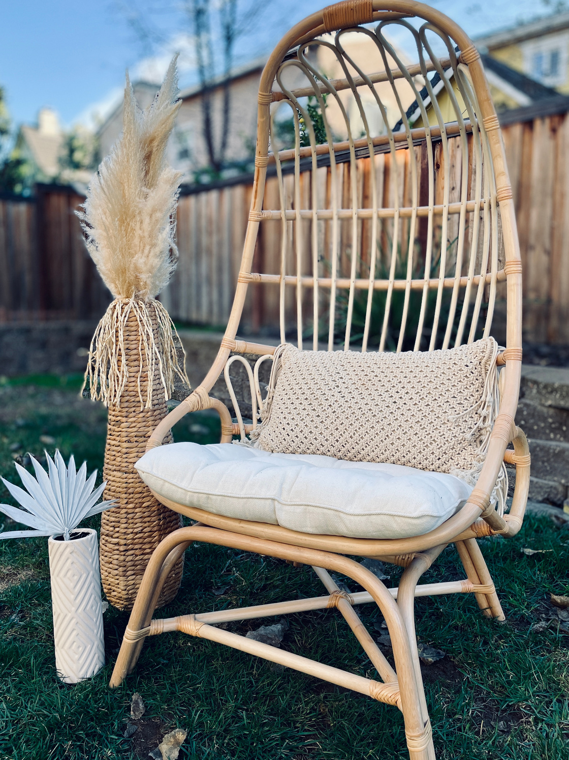 a rattan chair with pillows and a vase on the grass to rent. boho chair