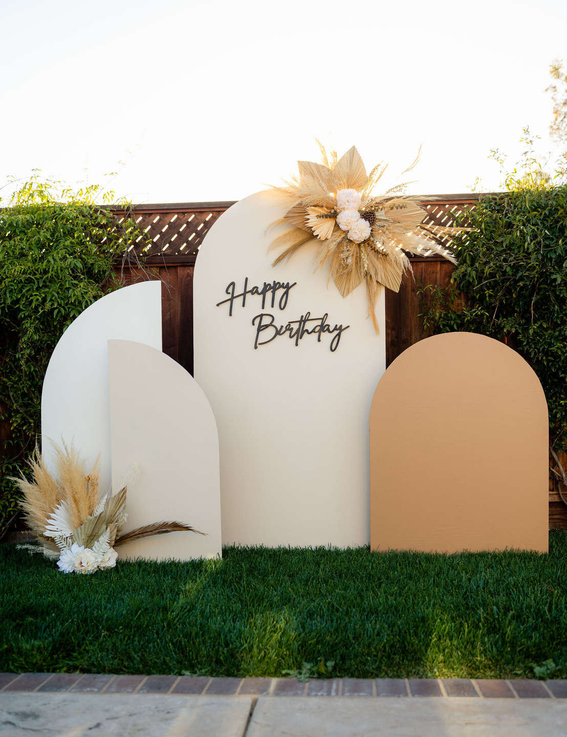 an outdoor birthday party with a arch backdrop, dried flowers, and a sign that says happy birthday. Can rent arches for all kinds of events
